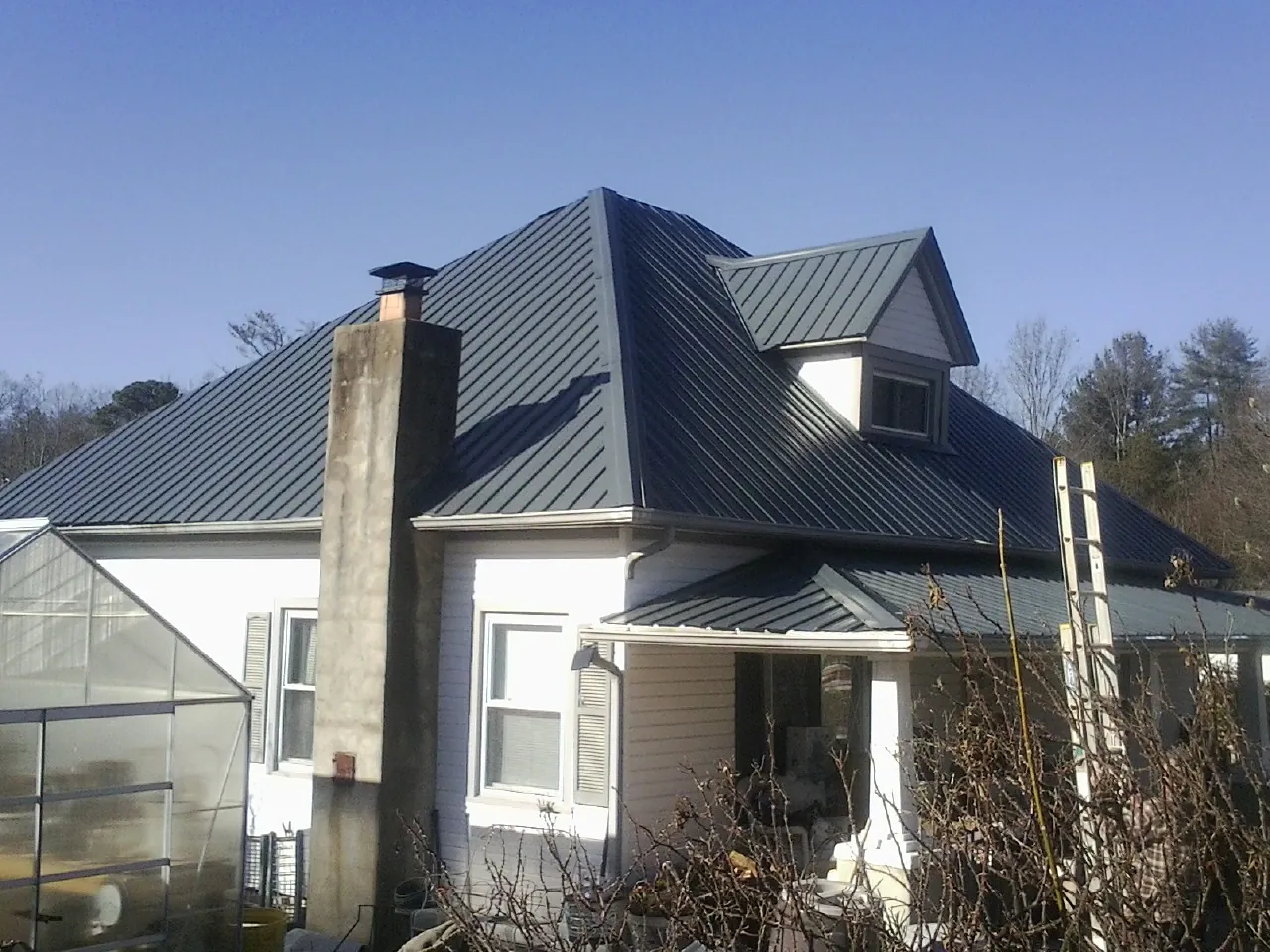 Dark blue standing seam metal roof on a white farmhouse with dormer — Slate & Tile Roof Repair by Roofing Brothers in Barrytown