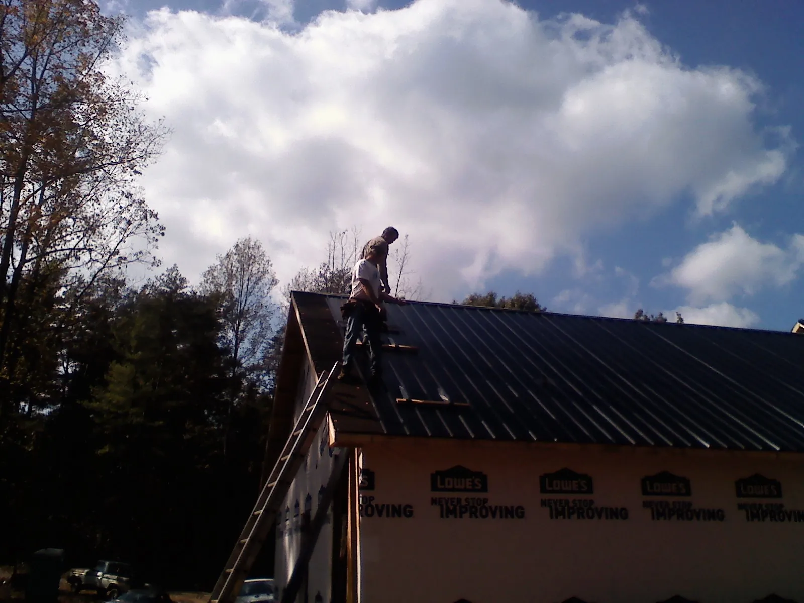 Roofer fastening dark metal panels high against a cloudy sky, from a Roof Inspection job in Barrytown