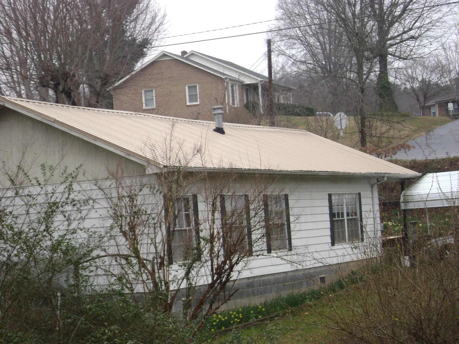 Tan metal roof on a white sided house set into a hillside — Commercial Roofing by Roofing Brothers in Barrytown